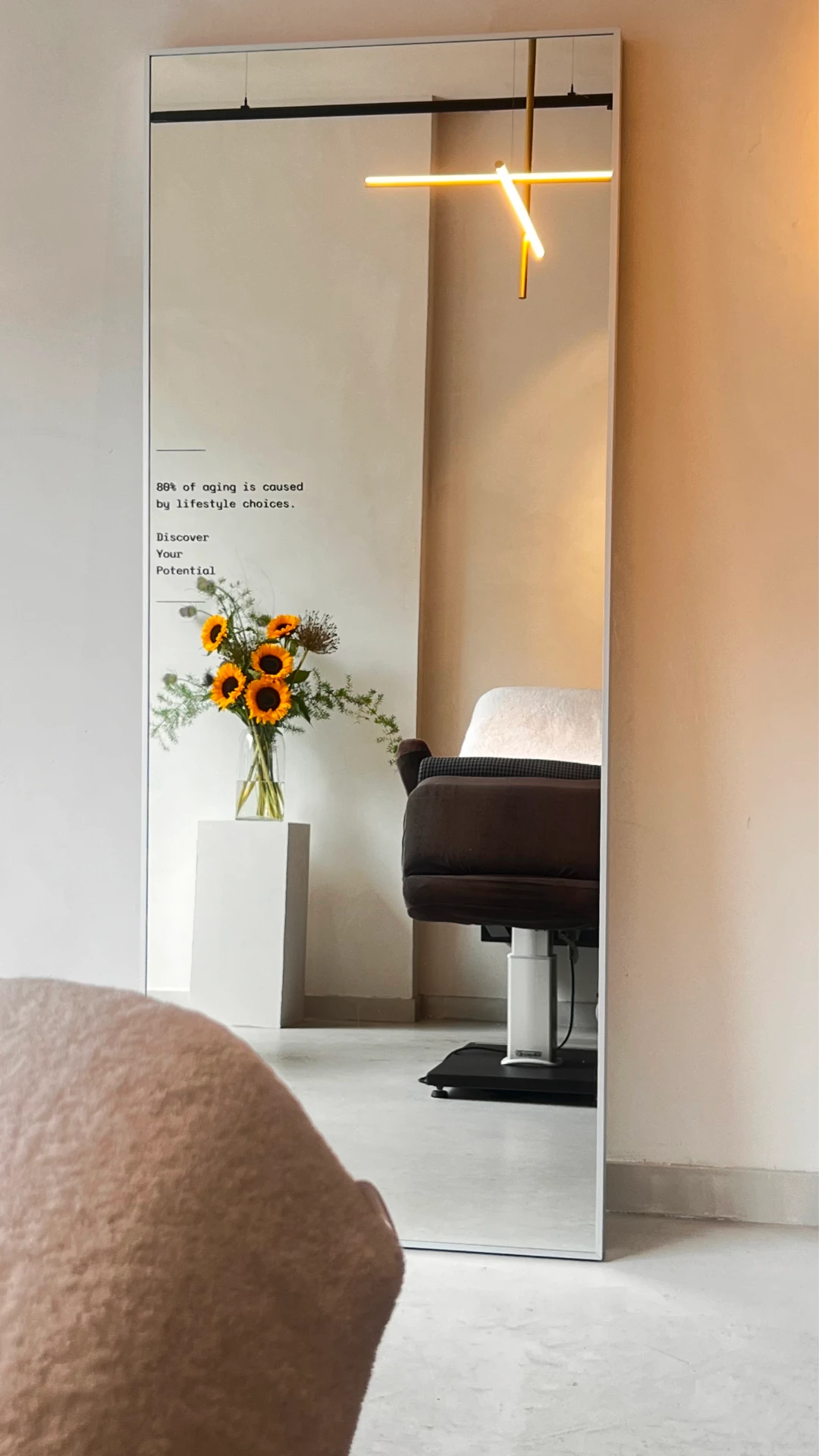 A modern mirror reflecting a treatment chair and a vase of vibrant sunflowers, creating a serene and welcoming atmosphere at Salon d’Homme.